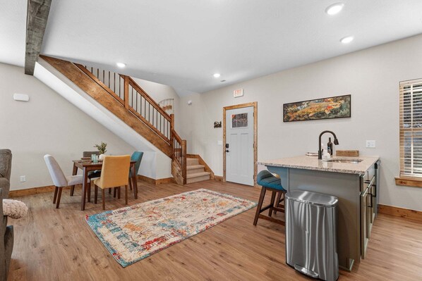 A modern kitchen with a wooden staircase, a dining area with chairs, and a kitchen island. - Private Hot Tub at The Bobber Stop, Arcade, Community Pools Nearby & Free Attraction Tickets (Hollister)