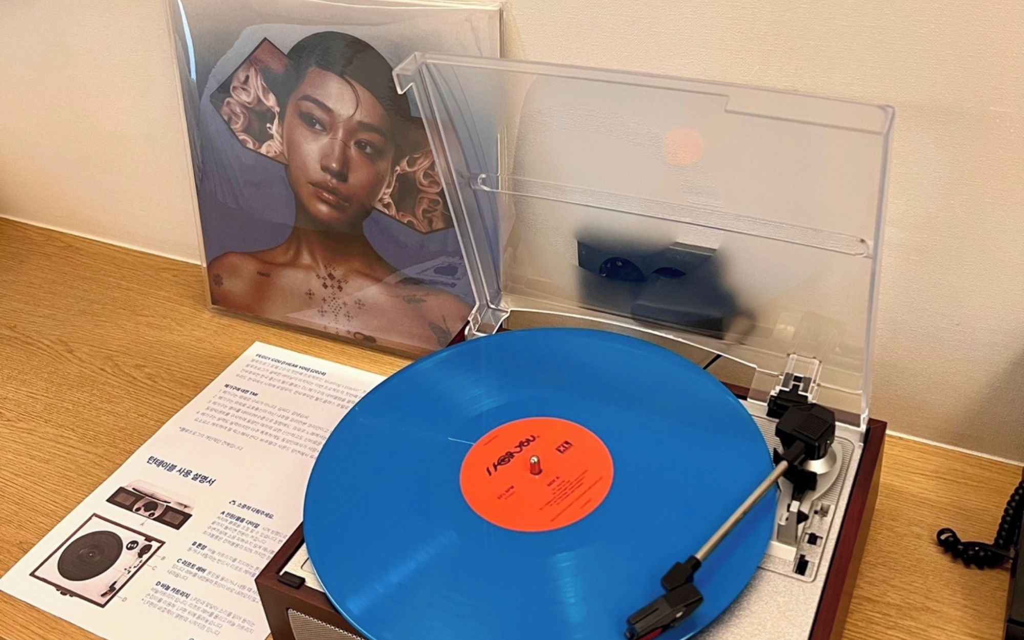A turntable with a blue record, a music player, and a framed picture on a wooden surface.