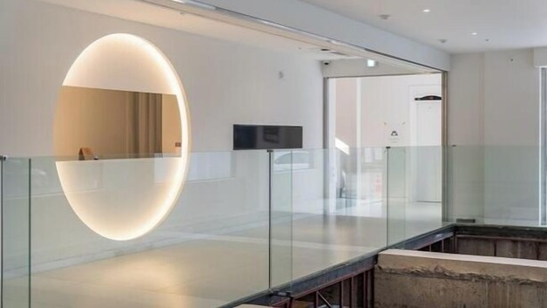 A modern hotel lobby with a glass railing, a large oval-shaped light fixture, and a flat-screen TV mounted on the wall. - BLUEFROG HOTEL (Incheon)