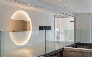A modern hotel lobby with a glass railing, a large oval-shaped light fixture, and a flat-screen TV mounted on the wall. - BLUEFROG HOTEL (Incheon)