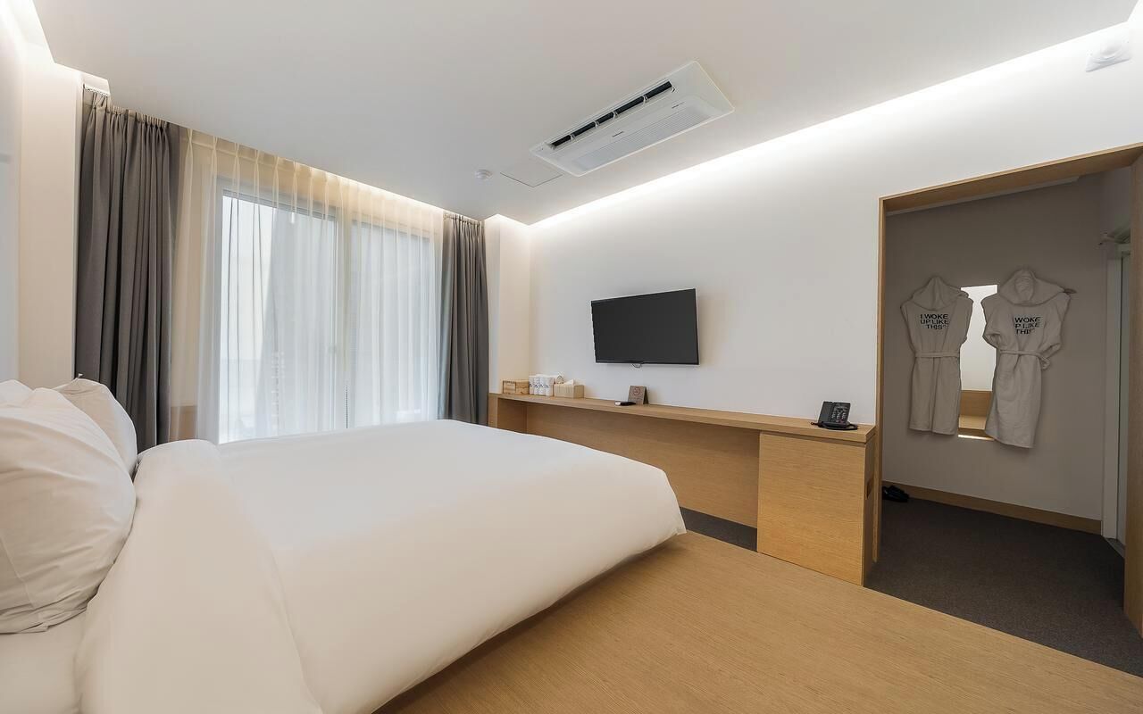 A hotel room with a large bed, a flat-screen TV mounted on the wall, a wooden desk, and a wardrobe with a mirror.