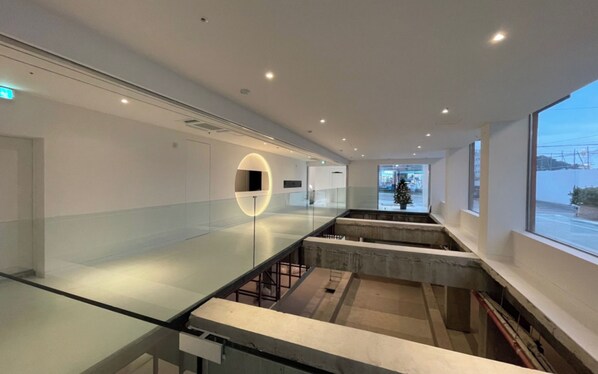 A modern interior with a glass railing, a circular light fixture, and a view of the outside. - BLUEFROG HOTEL (Incheon)