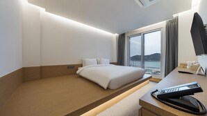 A hotel room with a bed, a desk with a telephone, a window with a view of the sea, and a flat-screen TV. - BLUEFROG HOTEL (Incheon)