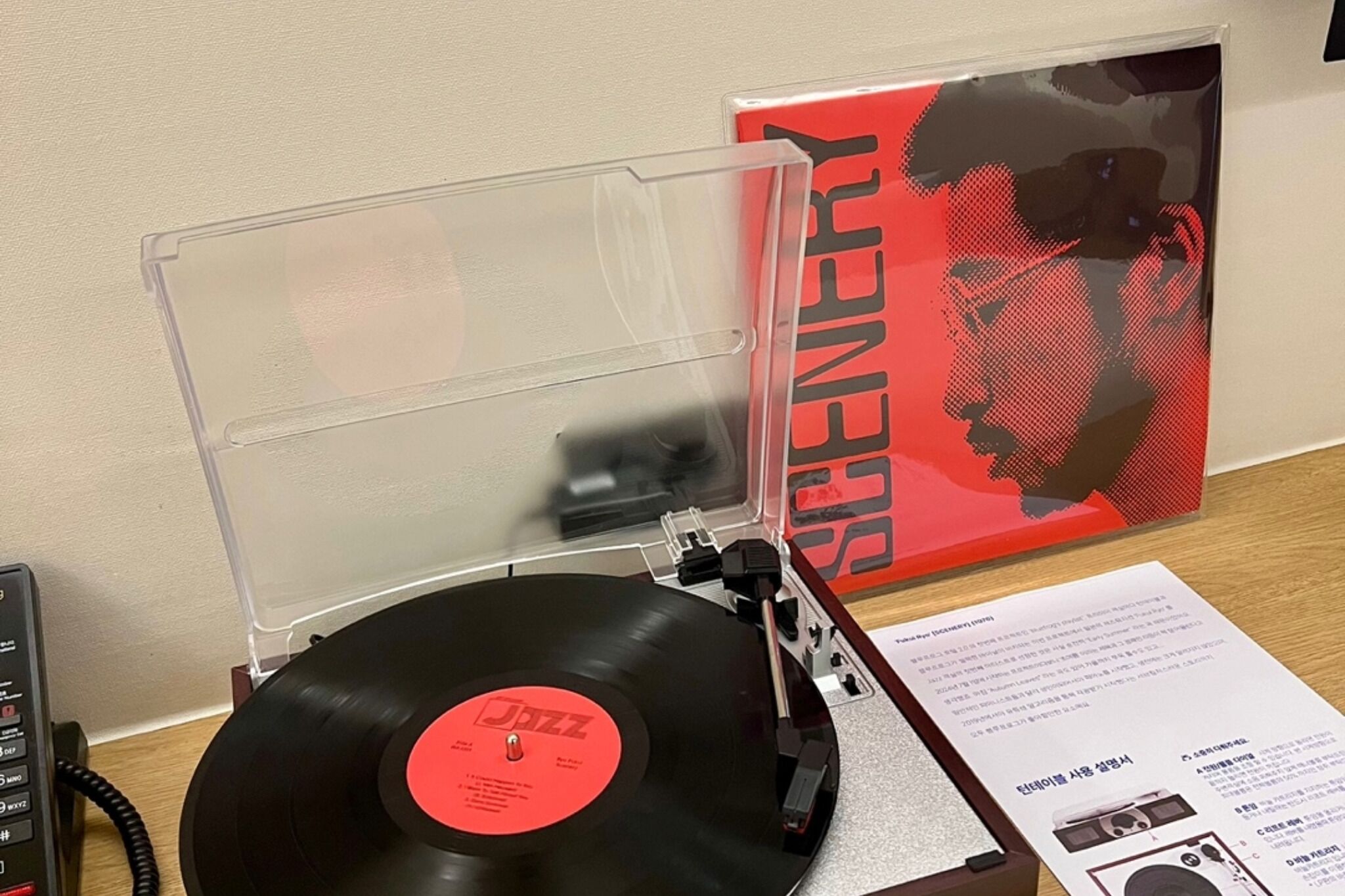 A turntable with a vinyl record, a DJ mixer, and a poster on a table.