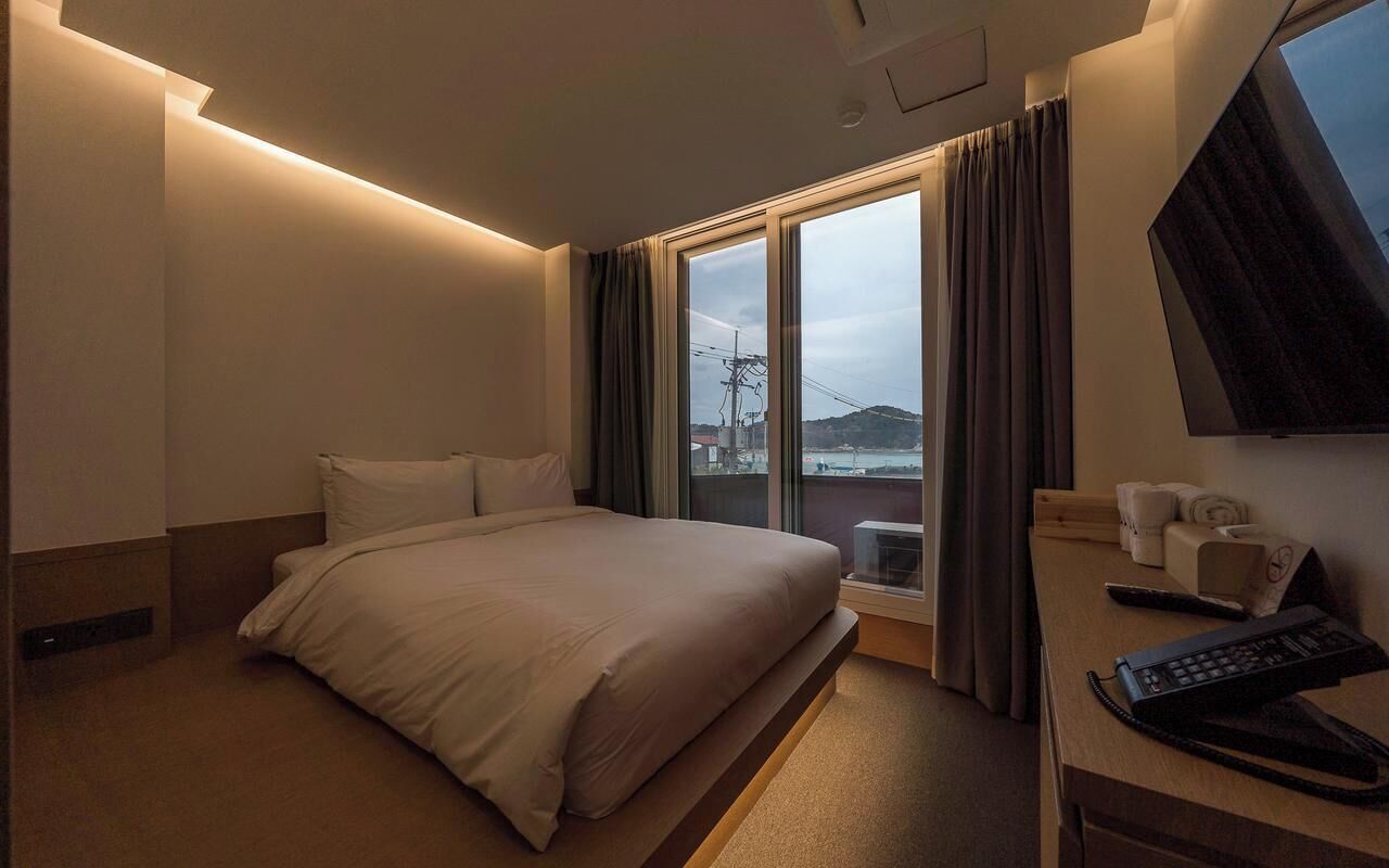 Habitación de hotel con cama, escritorio, computadora, teléfono, televisión y ventana con cortinas.