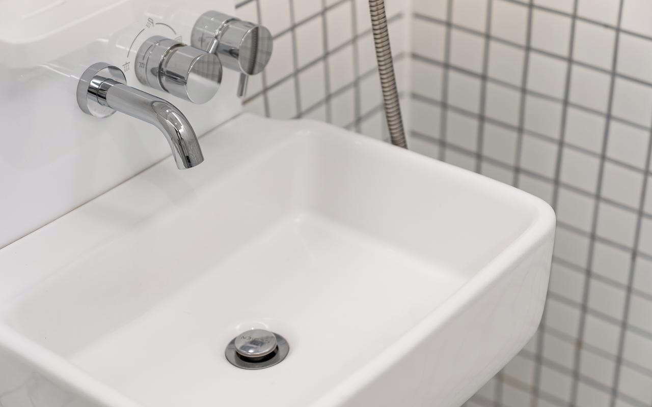 Un lavabo de salle de bain blanc, doté d’un robinet chromé et d’un tuyau de douche.