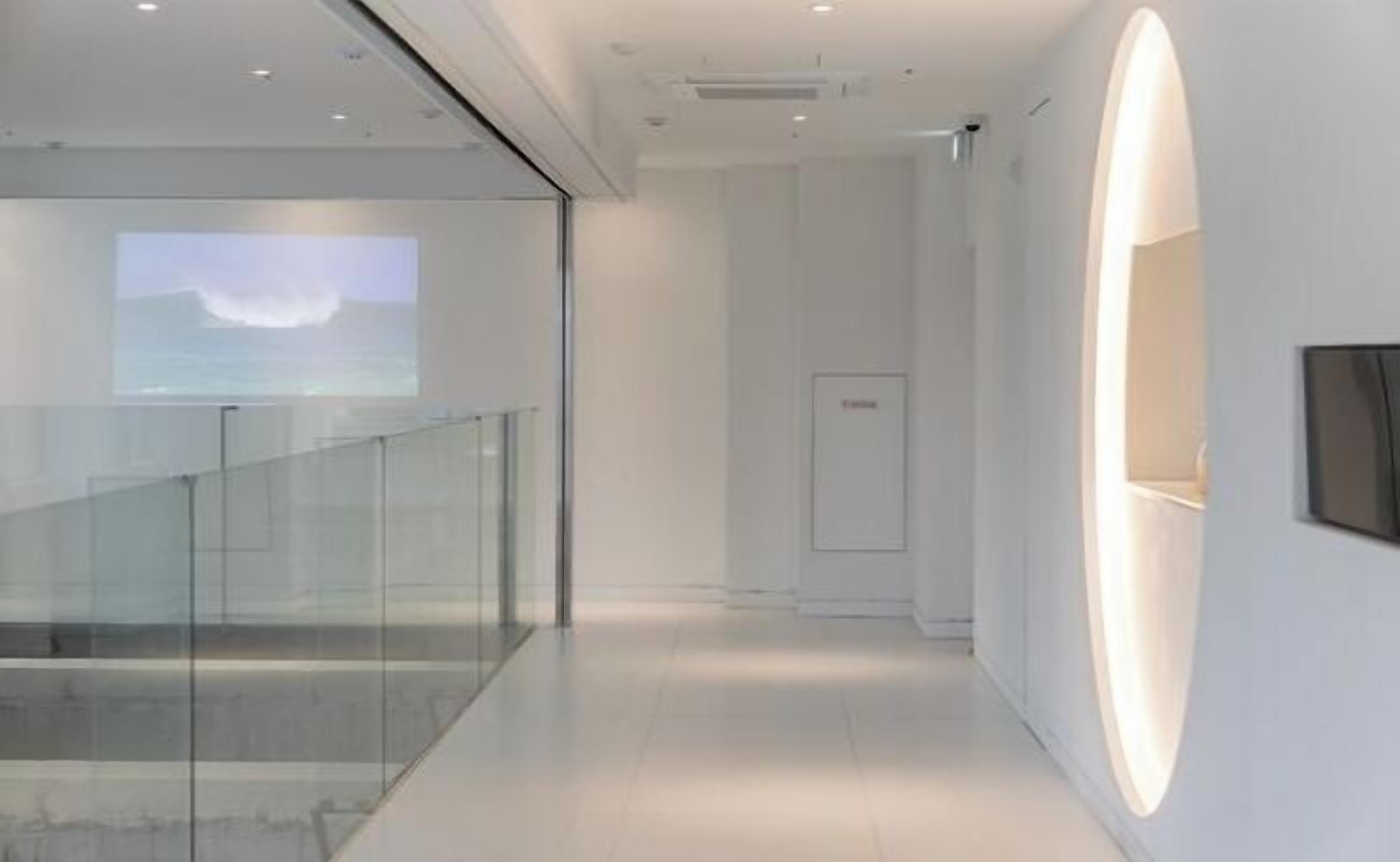 A modern interior with a glass railing, a projection screen, and a large illuminated wall.