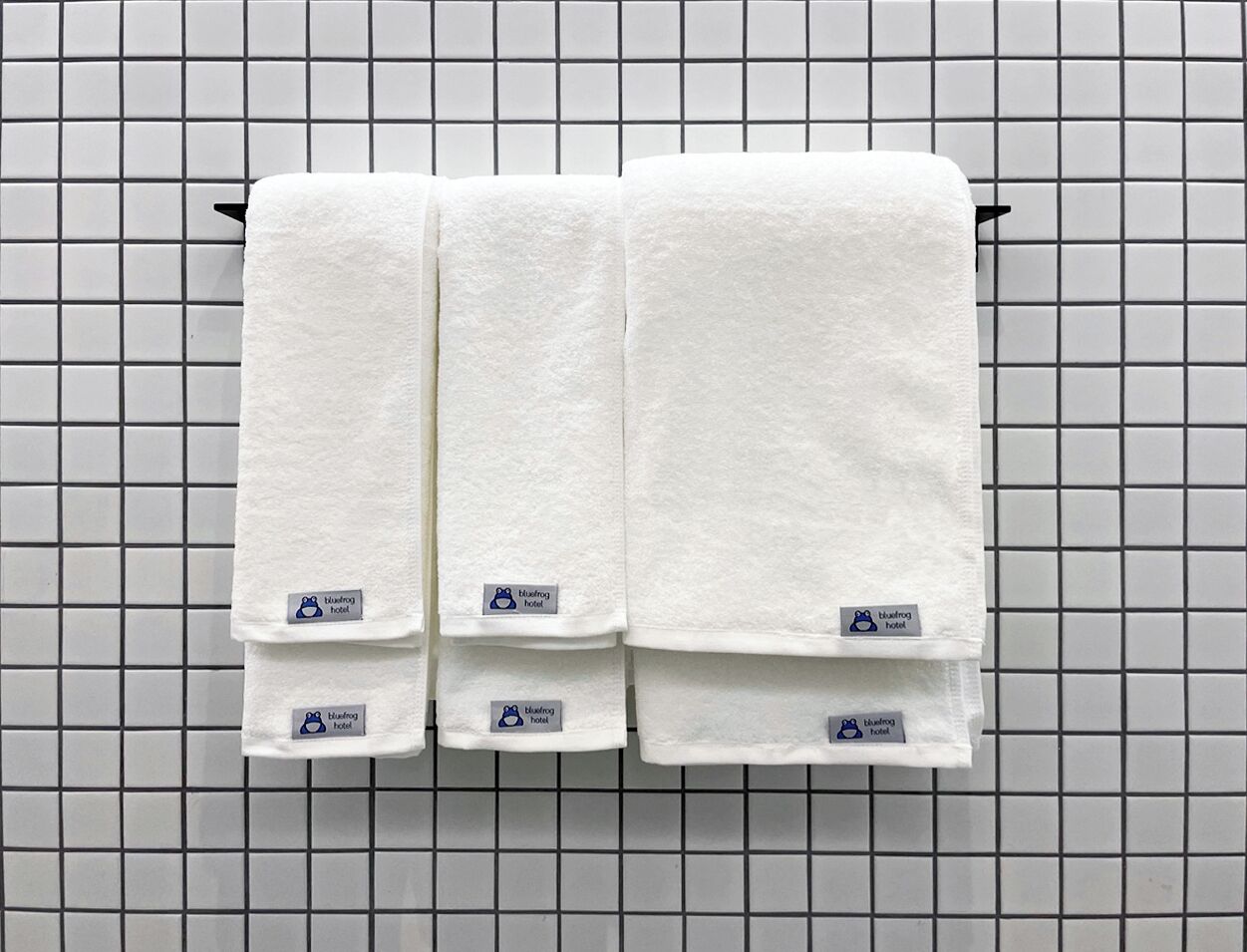Three white towels hanging on a rack against a tiled wall.