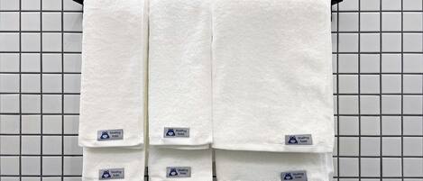 Three white towels hanging on a rack against a tiled wall.