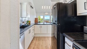 A modern kitchen with white cabinetry, a black refrigerator, and a wooden countertop. - Lakeview Home on Beaver with Balcony near DT Rogers (Rogers)