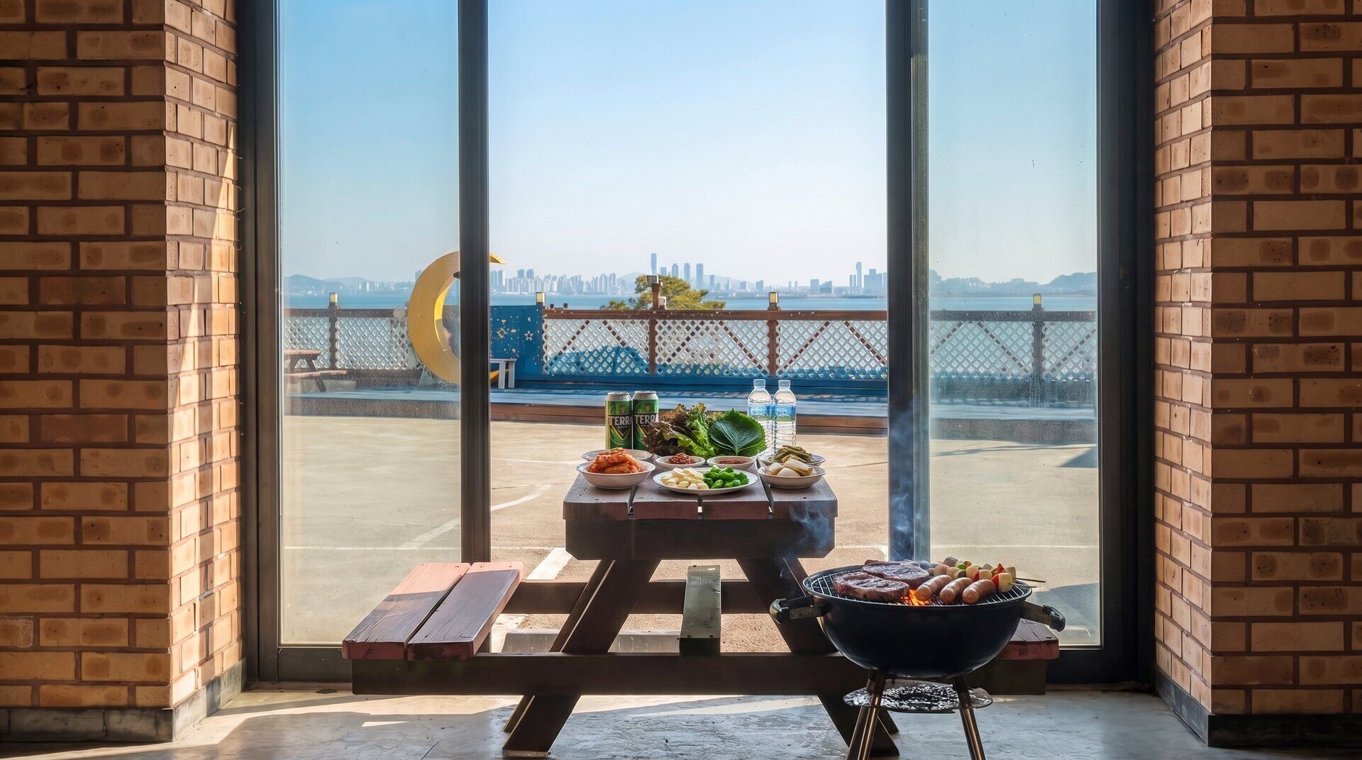 Eine Terrasse mit Grill, Picknicktisch und Lebensmitteln mit Blick auf ein Wasserufer und eine Stadtansicht.