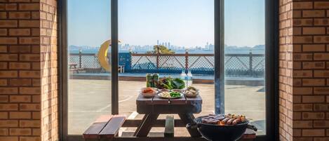 Un patio con griglia, tavolo da picnic e cibo, con vista su un lungomare e sullo skyline di una città.