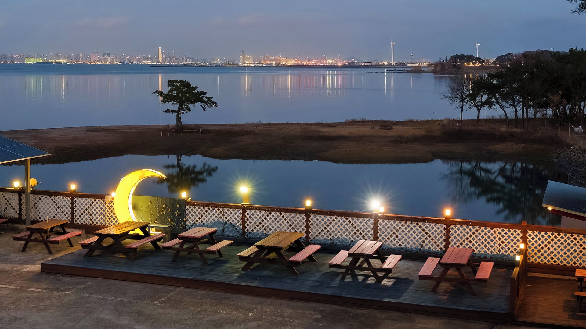 Une terrasse au bord de l’eau, dotée de tables de pique-nique et d’un luminaire en forme de croissant de lune.