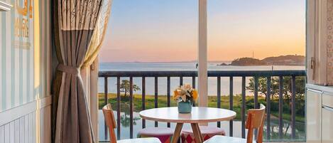 Un balcon avec une table et des chaises, une vue sur la mer et un rideau décoratif.