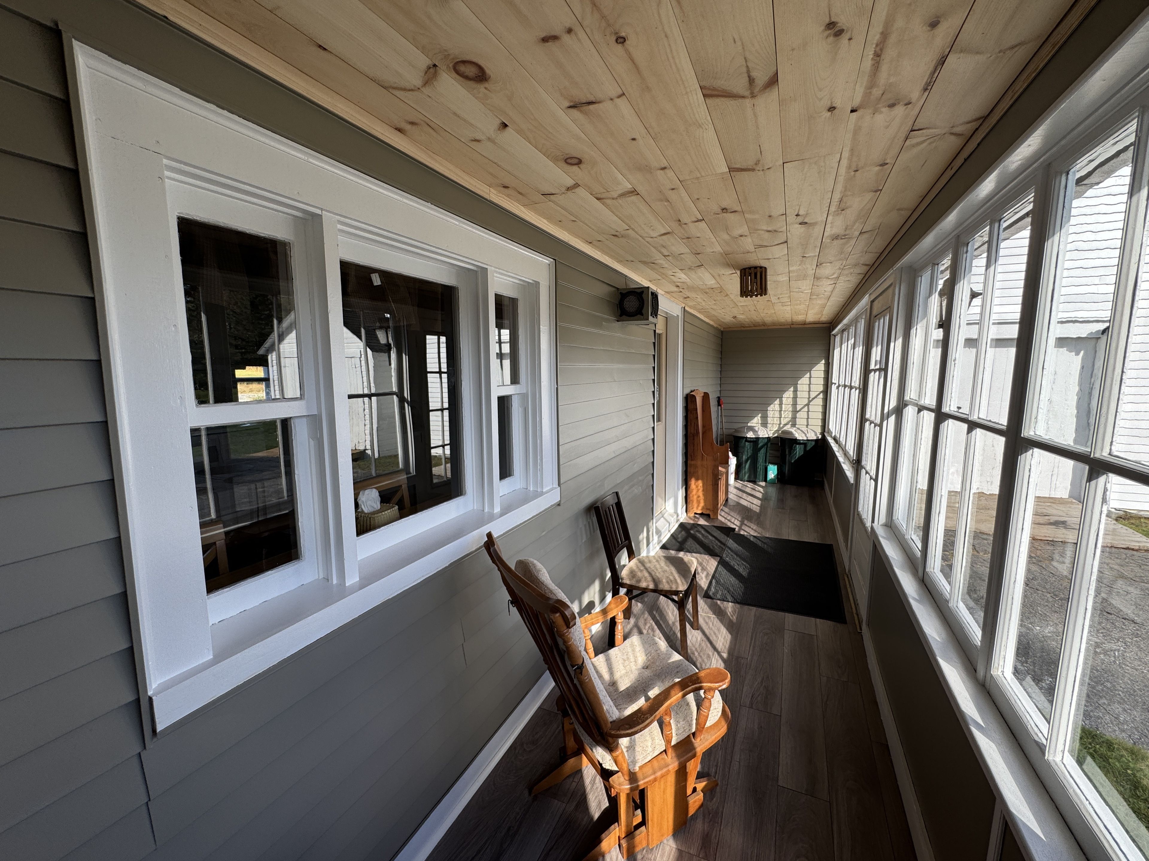A covered porch with a wooden ceiling, a bench, and a view of the street.