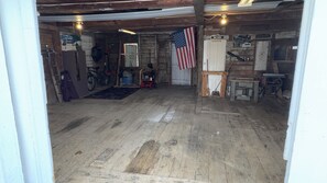 A garage with a wooden floor, an American flag, a bicycle, and a red lawnmower. - Charming 5-bedroom house in Jackman / Moose River perfect for families, groups. (Moose River)