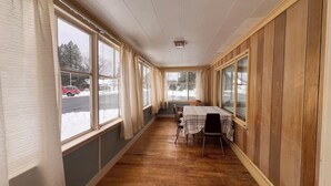 A room with a long wooden floor, large windows, and a table with chairs. - Charming 5-bedroom house in Jackman / Moose River perfect for families, groups. (Moose River)