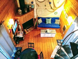 A cozy room with a wooden floor, a blue sofa, a small table with a tray, a fireplace, and a staircase. - The Perfect Getaway in Wellfleet (Wellfleet)