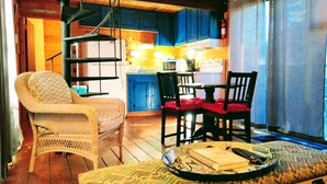 Un salon chaleureux avec un fauteuil en osier, une table à manger agrémentée de coussins rouges et un banc sur lequel est posé un plateau de nourriture.