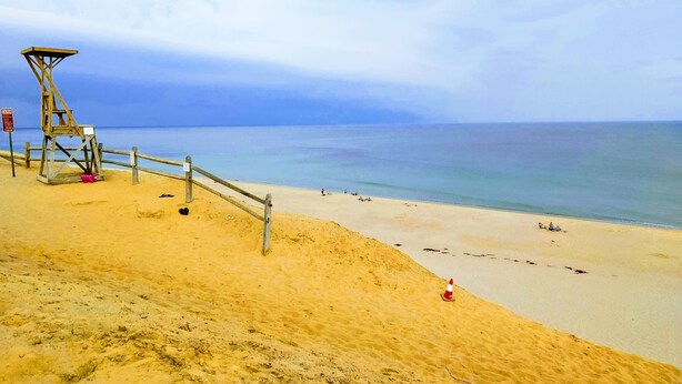 Une plage avec une tour de surveillance pour les sauveteurs, des dunes de sable et une vue dégagée sur l’océan.