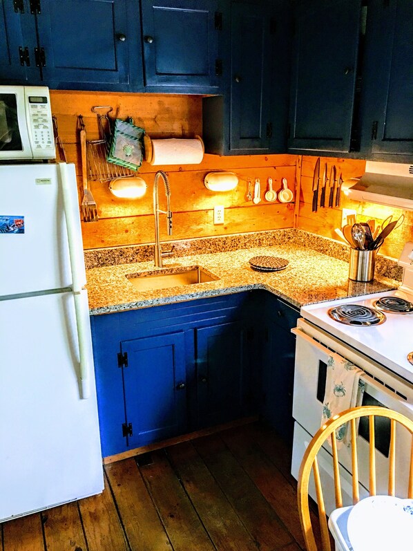 A compact kitchen with blue cabinets, a white refrigerator, a sink with a faucet, and a stove. - The Perfect Getaway in Wellfleet (Wellfleet)