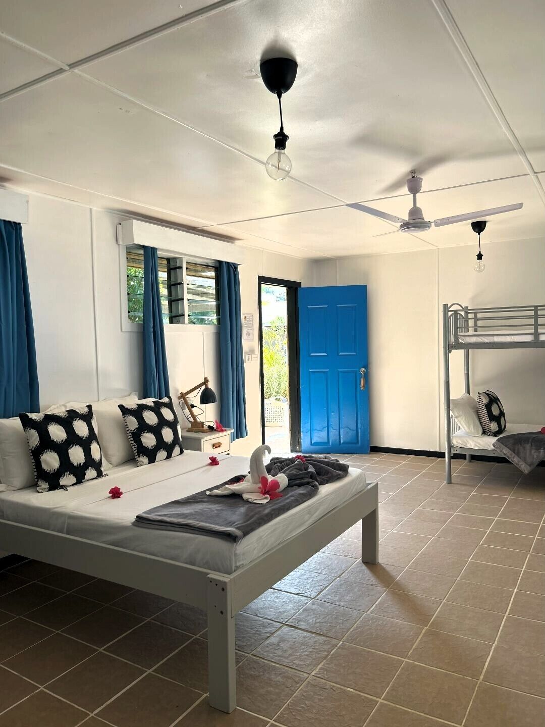 A room with a bed, a desk, a chair, a blue door, and a window with curtains.