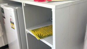 Ένα λευκό γραφείο με ένα κόκκινο λουλούδι, μια καφετιέρα και έναν κίτρινο φάκελο πάνω του.