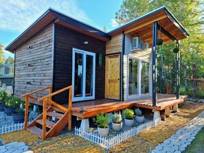 A modern wooden cabin with a wooden deck, a sliding glass door, and a small porch area.