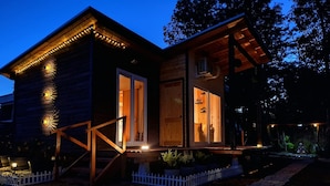 A wooden cabin with a porch, a staircase, and a small garden area.