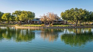 Un hotel sul lago con il suo riflesso nell'acqua, circondato da alberi e un cielo sereno.