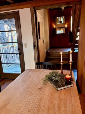 A wooden dining table with candles and greenery, a wooden staircase, and a view of a deck outside.