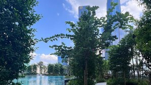 Un sentier mène à une piscine entourée d’une végétation luxuriante, avec des bâtiments modernes en arrière-plan.