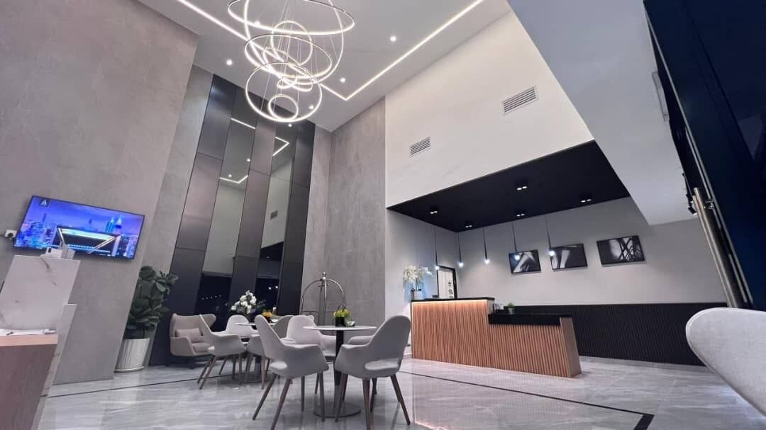 A modern hotel lobby with a reception desk, seating area, and a large TV screen.