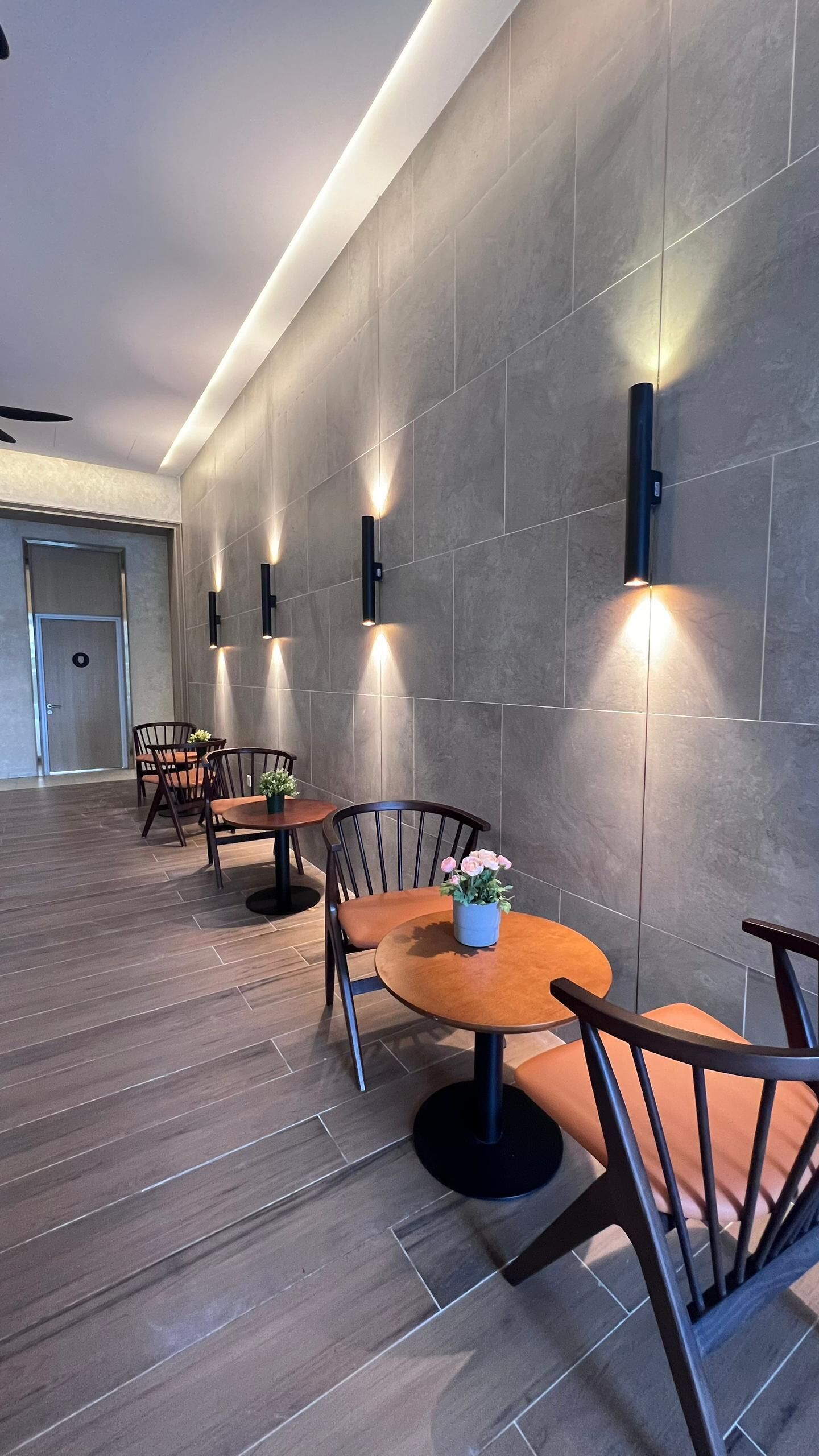 Un comedor moderno con mesas redondas y sillas de madera, iluminado por luces fijadas en la pared.