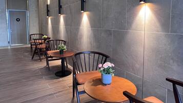 Un comedor moderno con mesas redondas y sillas de madera, iluminado por luces fijadas en la pared.