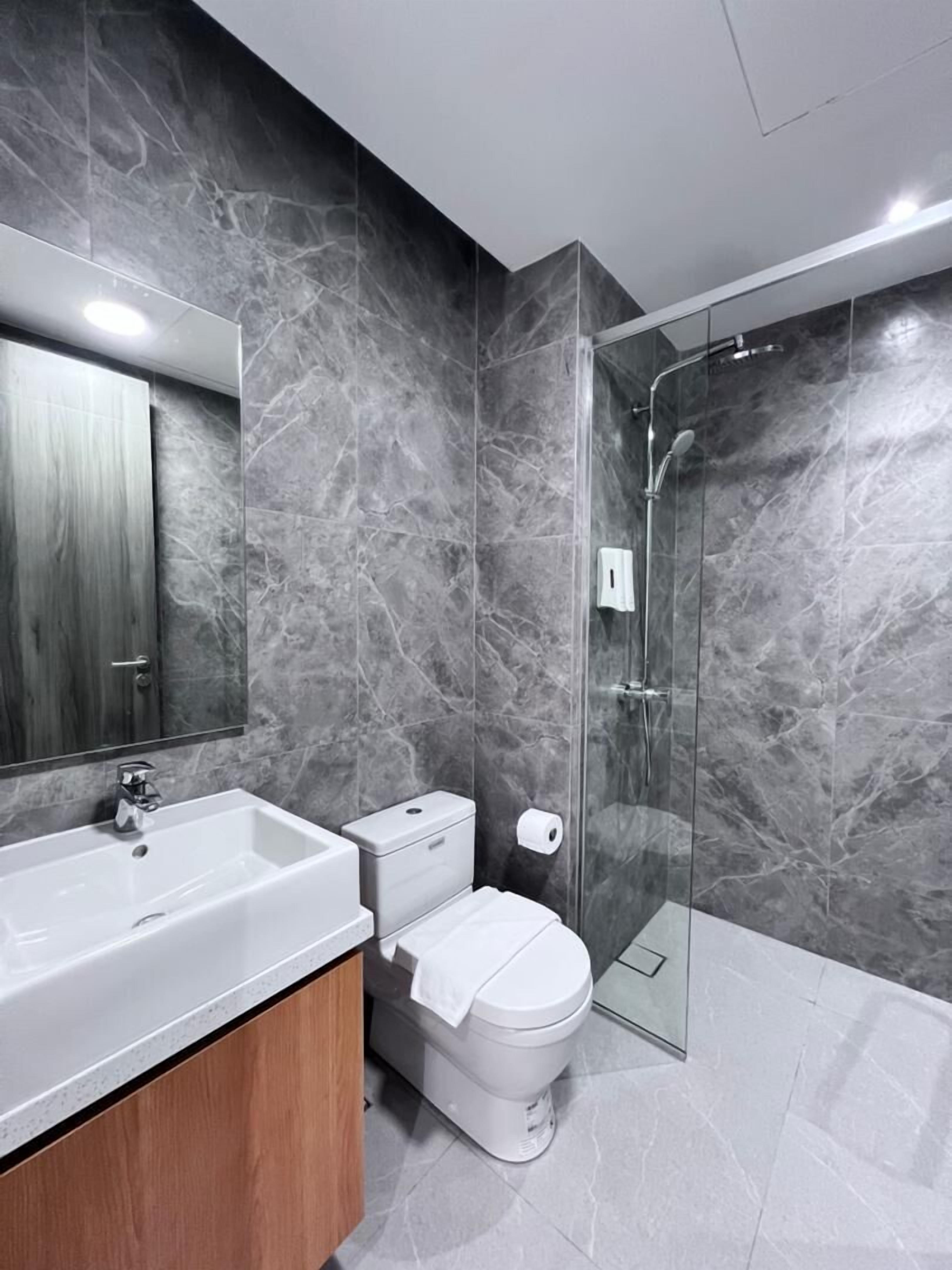 A modern bathroom with a marble wall, a white sink, a toilet, and a glass-enclosed shower.