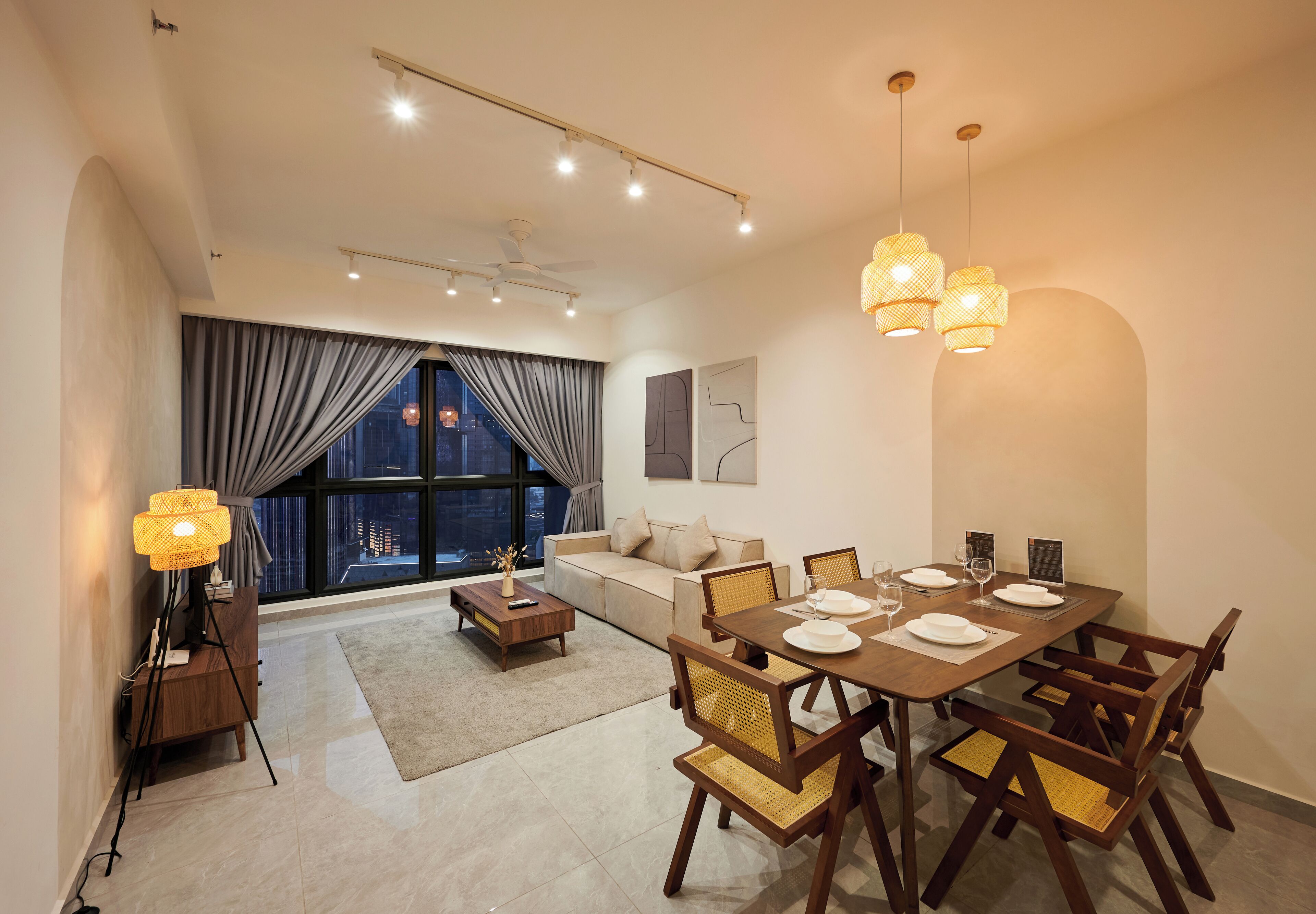 A modern living room with a dining area, large windows with curtains, a sofa, a coffee table, and a lamp.