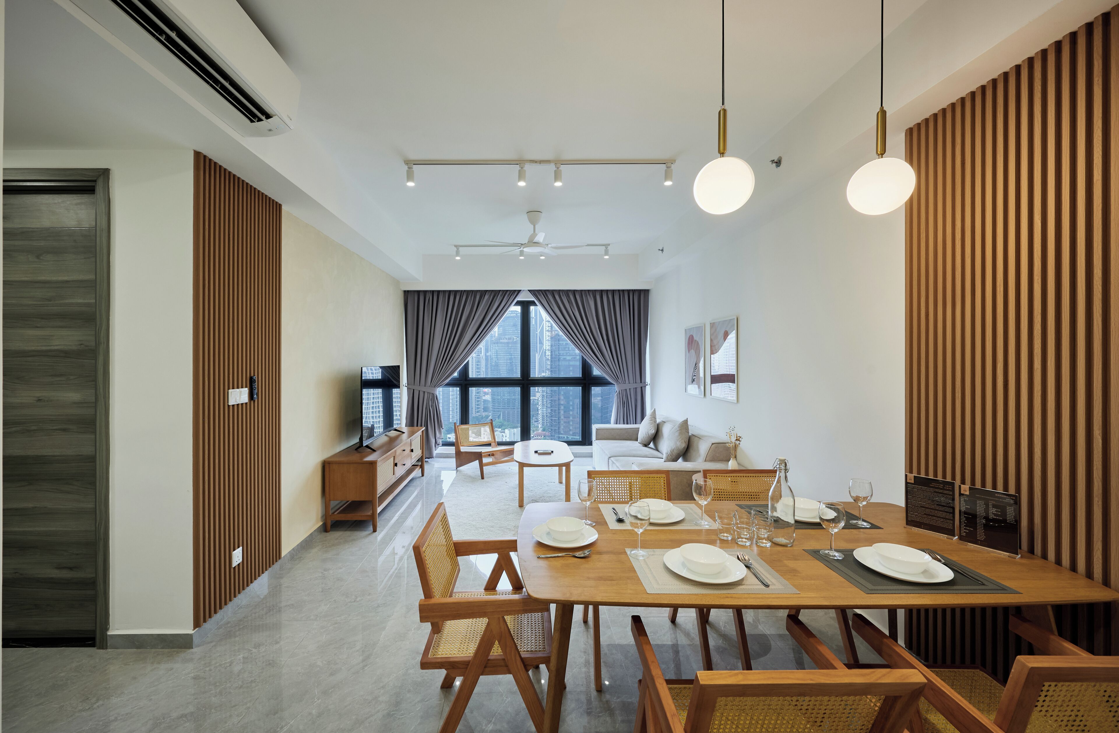 Un espace repas moderne avec une table en bois dressée pour quatre personnes, un canapé et un téléviseur en arrière-plan.