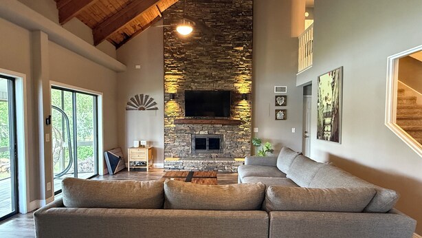 A spacious living room with a stone fireplace, a large sectional sofa, and a television mounted on the wall. - Lakefront Retreat Tampa, 7BR, Dock & Fun (Lutz)