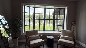 A room with a large bay window, two chairs, a small round table, and a potted plant. - Lakefront Retreat Tampa, 7BR, Dock & Fun (Lutz)