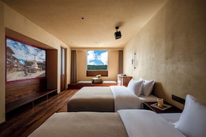 A hotel room with two beds, a large window, a painting on the wall, and a small table with a cup and a book.