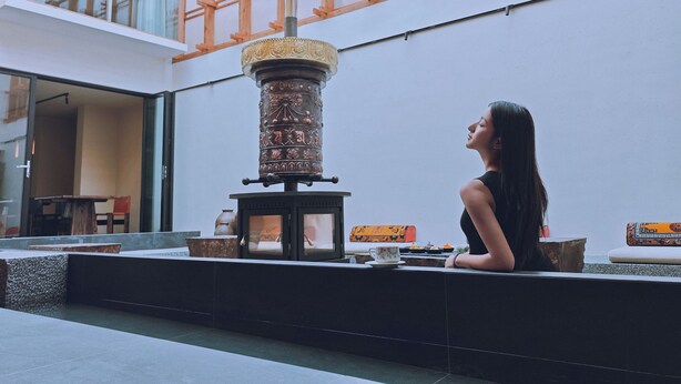 A woman sitting by a decorative pillar in a spacious indoor area with a high ceiling and a skylight. - Shangri-La Nazhu Tibetan Mansion Hotel (Deqin)