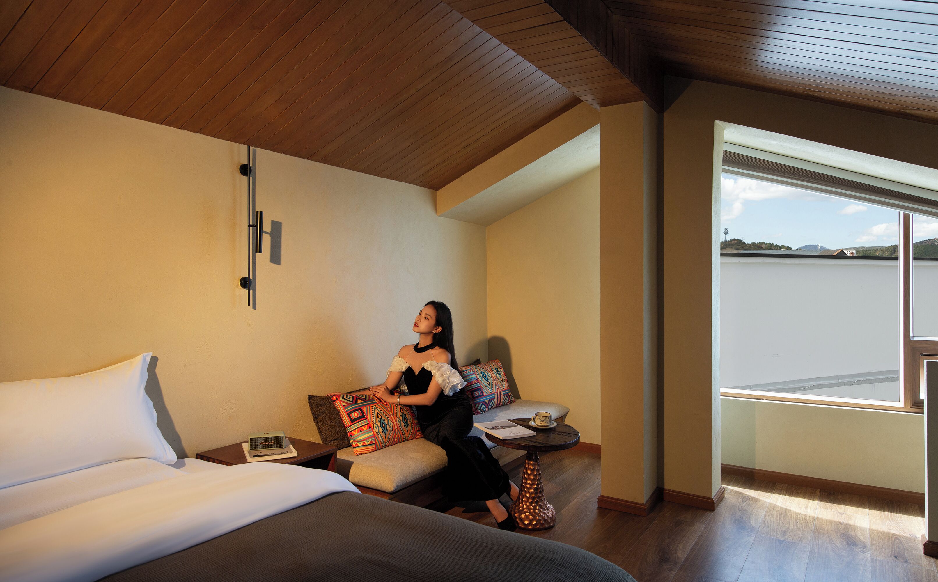 A modern hotel room with a bed, a small table, and a view of a body of water through a large window.