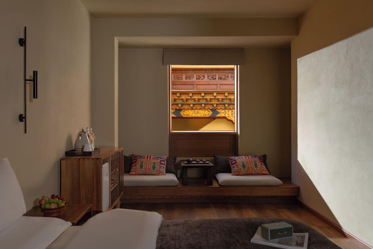Um quarto aconchegante com um banco de madeira, uma mesa pequena e uma janela decorativa.