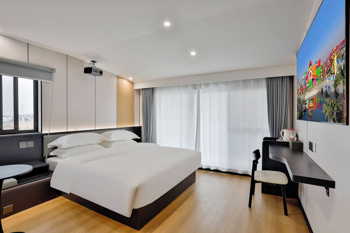 A modern hotel room with a large bed, a desk, and a projector.