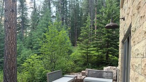 A patio with two wooden benches and a table, surrounded by a stone wall and a view of a forest.