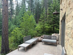 Eine Terrasse mit zwei Holzbanken und einem Tisch, umgeben von einer Steinmauer und Blick auf einen Wald.