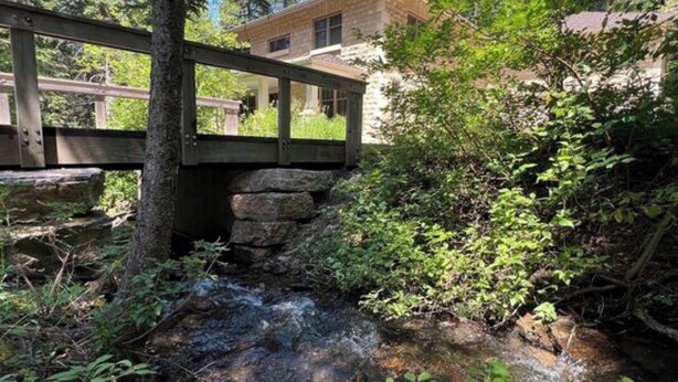 A stone bridge over a stream with a house in the background.