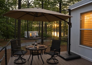 A deck with a table and chairs, an umbrella, and a small house in the background.