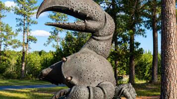 A sculpture of a large, textured creature with a prominent mouth and claws, set on a circular base in a natural setting with trees and a clear sky.
